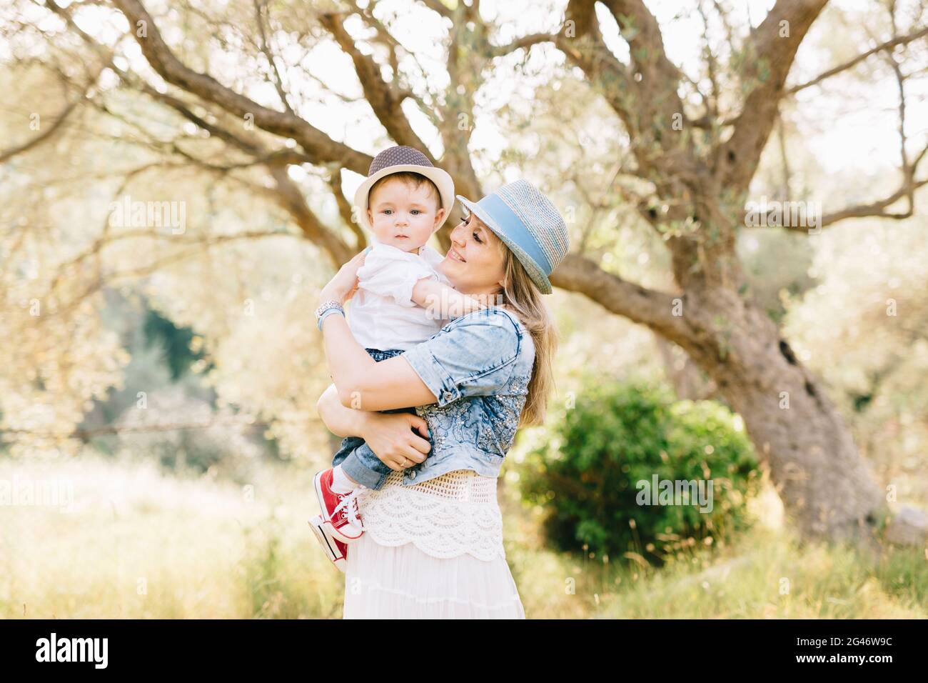 Mutter hält ihren Sohn in den Armen vor dem Hintergrund Von einem schönen Baum in einem Olivenhain Stockfoto