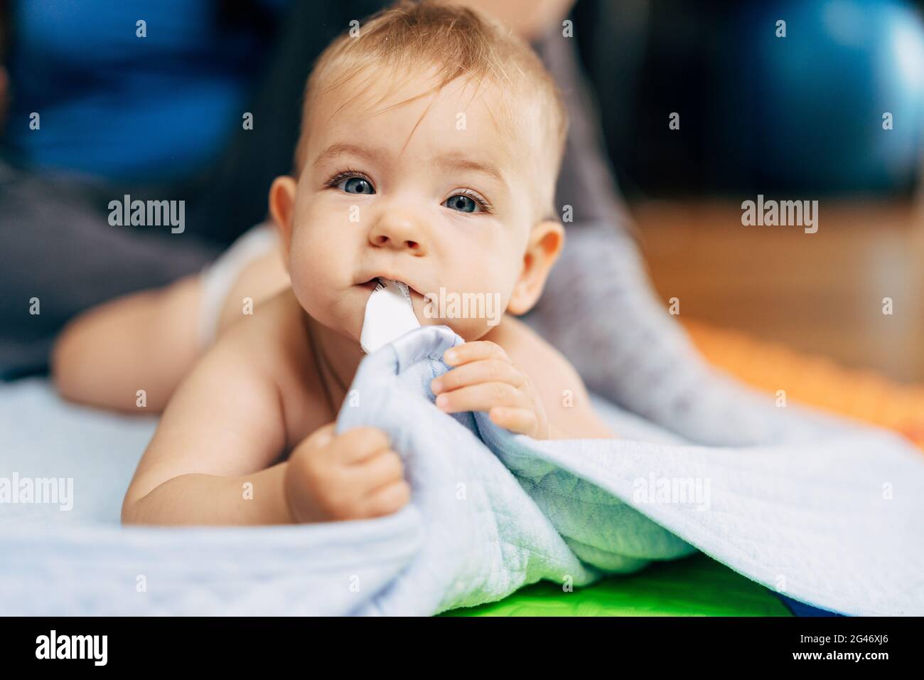 Kleines Baby in Windeln liegt mit seinem Bauch auf einem Blaue Decke und hält den Rand mit seinen Händen und Zähne Stockfoto