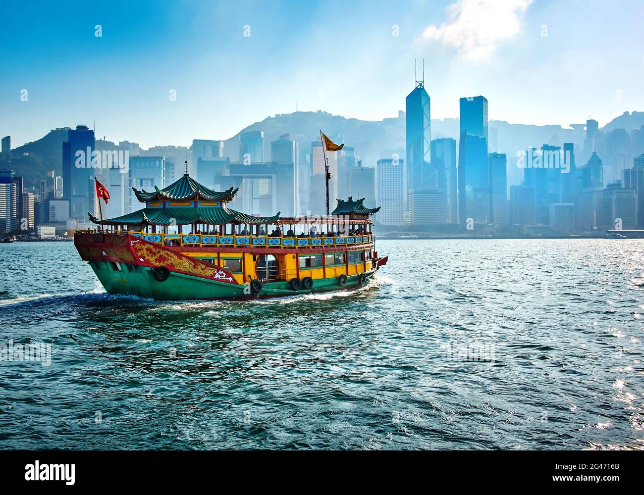 Passagierfähre, die Menschen zwischen den Inseln von Hong Kong mit Wolkenkratzern im Hintergrund transportiert Stockfoto