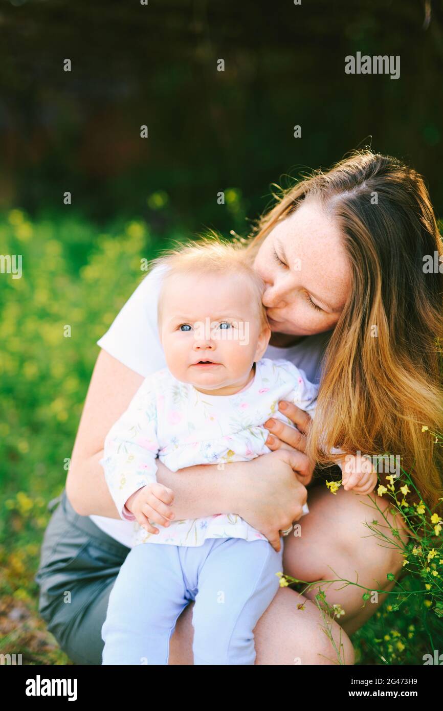 Mutter küsst ihr Baby Mädchen, während sie auf der sitzt Rasen Stockfoto