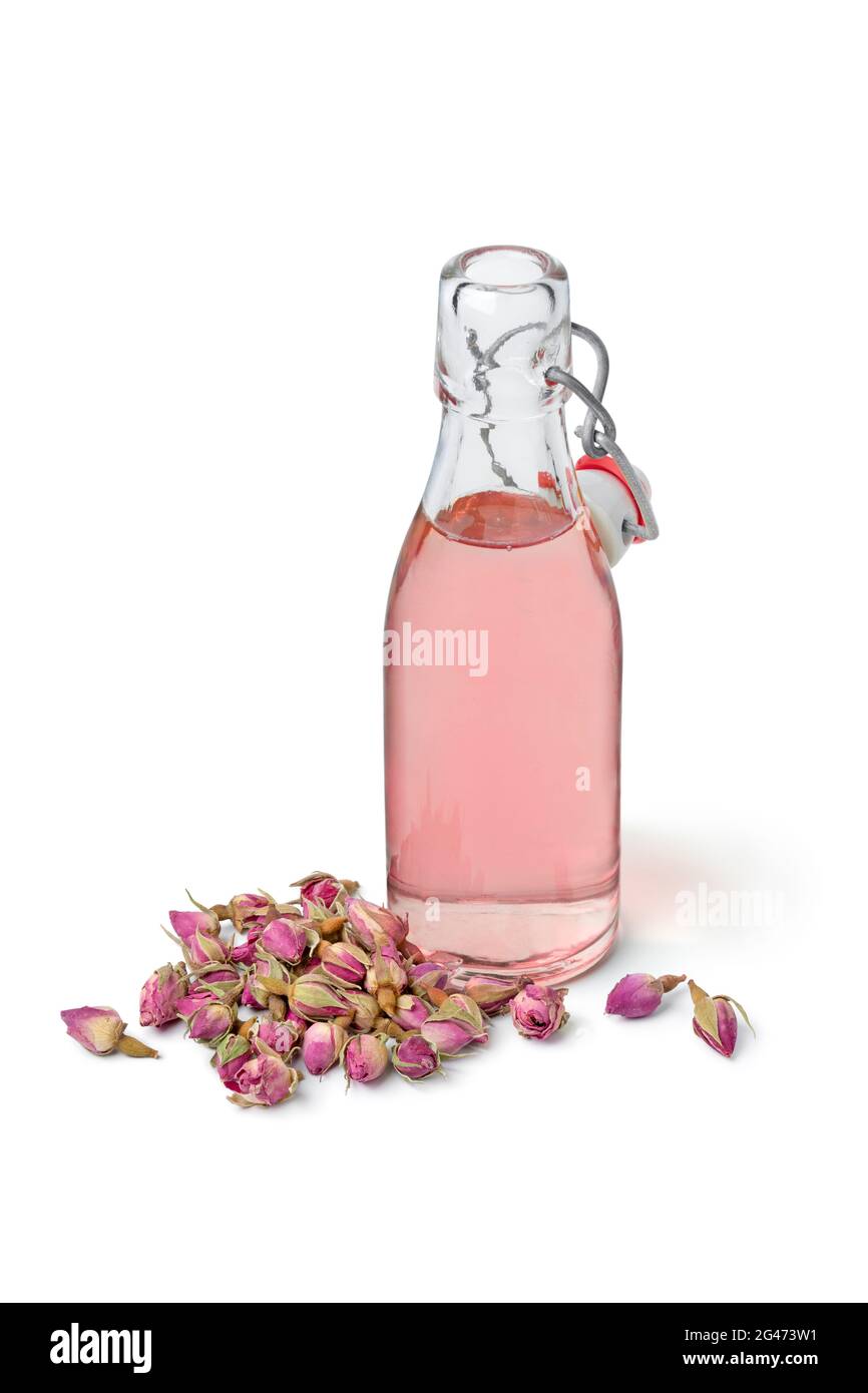 Aromatisches Rosenblütler-Wasser in einer Glasflasche mit getrockneten Rosenblüten vorne isoliert auf weißem Hintergrund Stockfoto