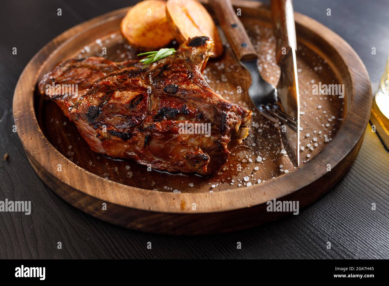 Mittelselten Steak auf Knochen Kalbsrippe mit Kartoffeln auf einem Holzteller Stockfoto