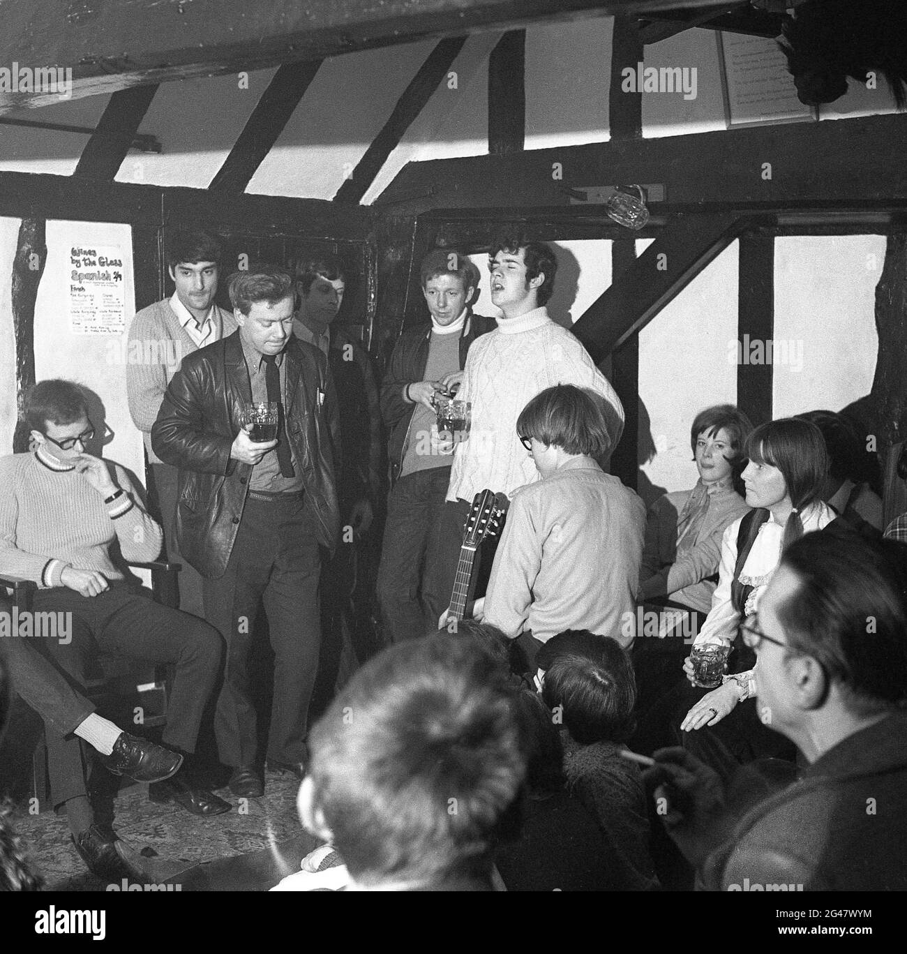 1970, historische Volksmusik, in einem Raum in einem hölzernen, gestrahlten Country Pub, ein Publikum, das einem jungen Mann in einem Wollpullover mit Rollkragen lauscht, sein Pint Besen ausstanzt und ein Lied im Castle Inn, Colchester, Essex, England, Großbritannien, singt. Stockfoto