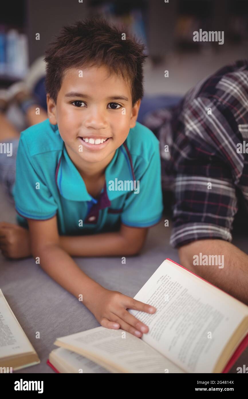 Porträt eines glücklichen Schuljungen beim Lesen von Büchern in der Bibliothek Stockfoto