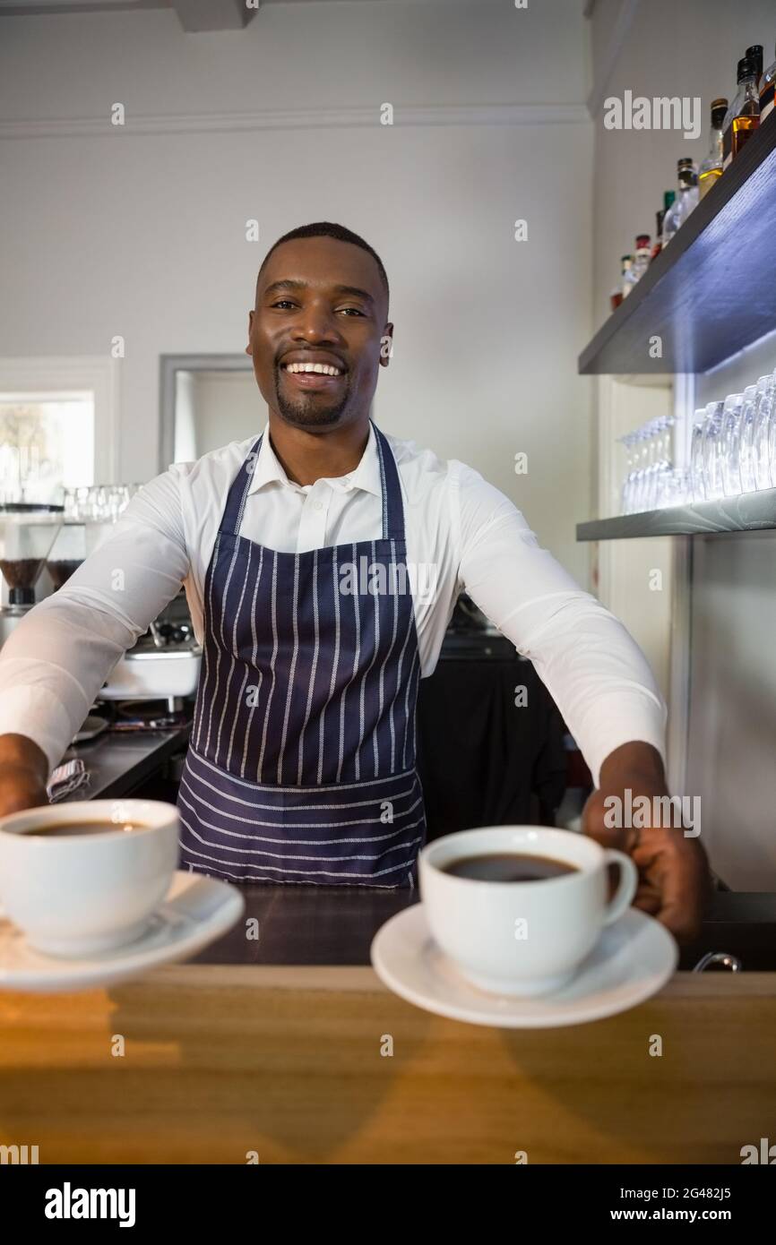 Porträt eines glücklichen Kellners, der im Café Kaffeetassen gab Stockfoto