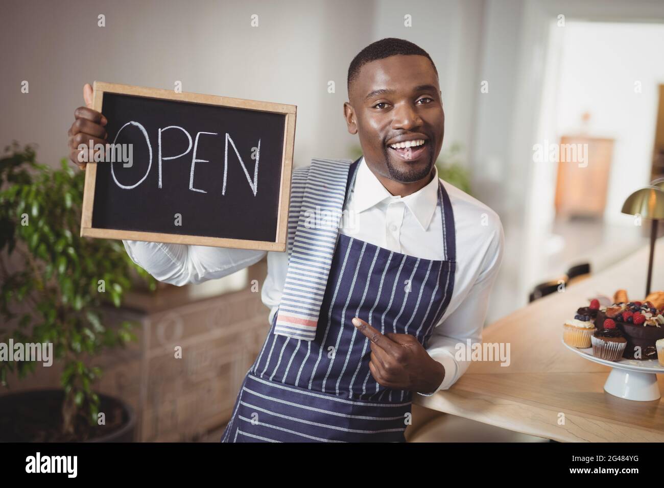 Lächelnd Kellner zeigt Tafel mit Schild "geöffnet" Stockfoto