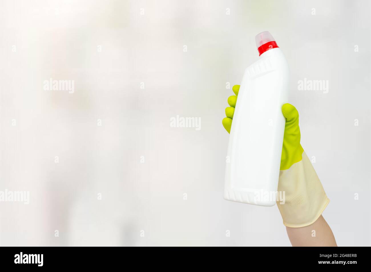 Frühjahrsputz-Konzept. Weiße Flasche mit flüssigem Reinigungsmittel in der Hand mit gelben Gummihandschuhen. Das Konzept des Reinigungsservice Stockfoto