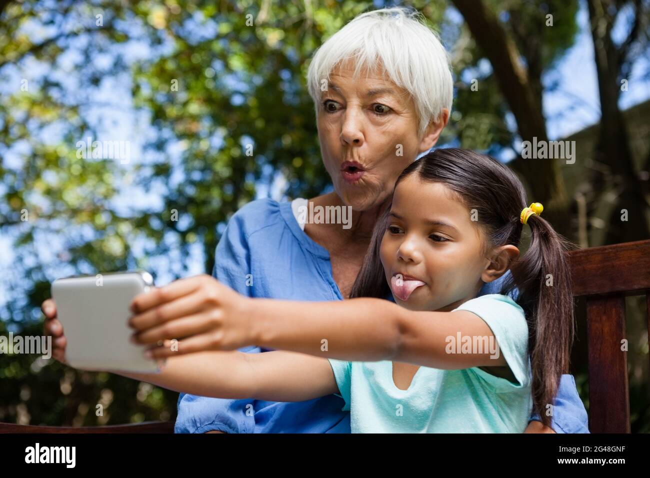 Großmutter und Enkelin machen sich beim Selfie auf der Bank ein Gesicht Stockfoto