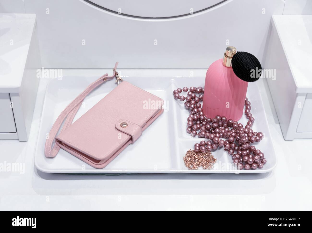 Kosmetiktisch mit rosa Clutch, Parfüm und Perlen. Stockfoto