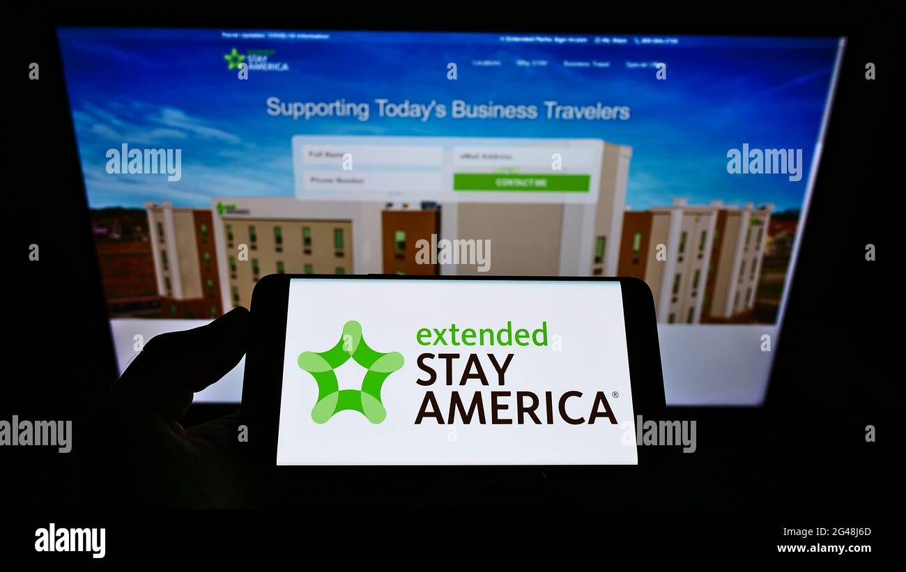 Person mit Mobiltelefon und Logo der US-Apartmenthotelkette Extended Stay America Inc. Auf dem Bildschirm vor der Webseite. Konzentrieren Sie sich auf die Telefonanzeige. Stockfoto