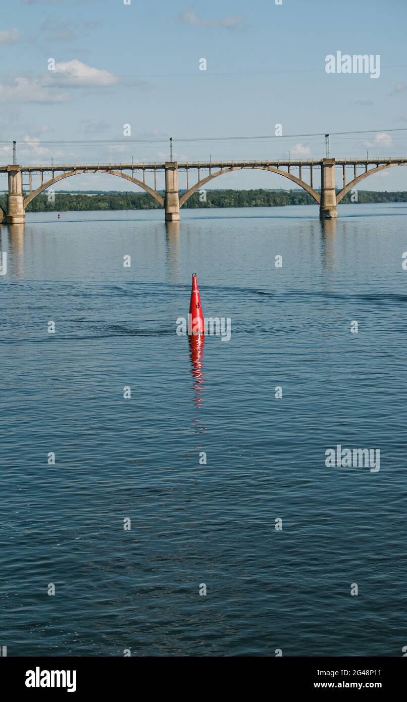 Schwimmende rote Navigationsboje auf blauem Wasser des Dnipro River. Boje im Fluss. Navigationsausrüstung. Ruhige Wasseroberfläche. Stockfoto
