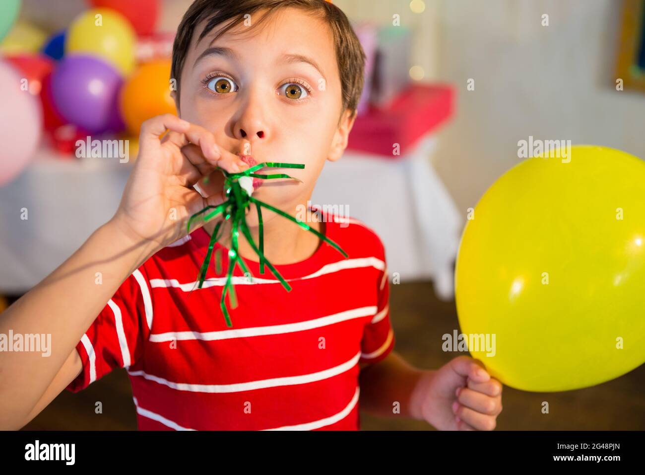 Niedlicher Junge weht Party Horn während der Geburtstagsfeier Stockfoto