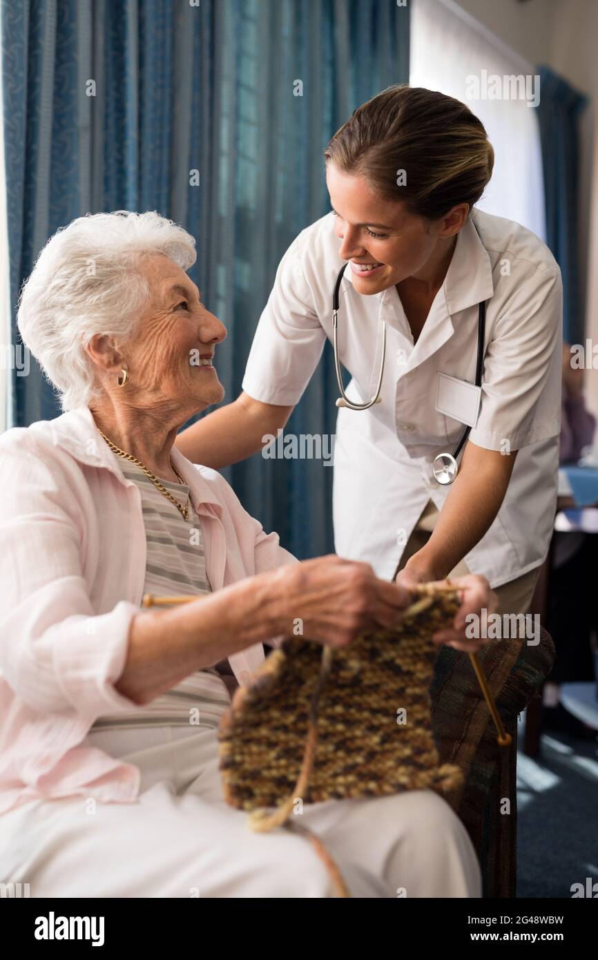 Lächelnde ältere Frau strickt, während sie eine Ärztin anschaut Stockfoto