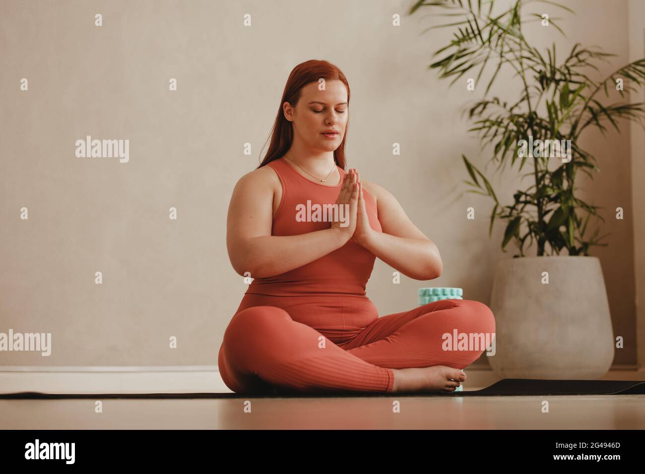 Frau, die zu Hause arbeitet, Yoga-Übungen auf der Matte macht. Fitness-Frau meditiert in Lotusstellung. Stockfoto