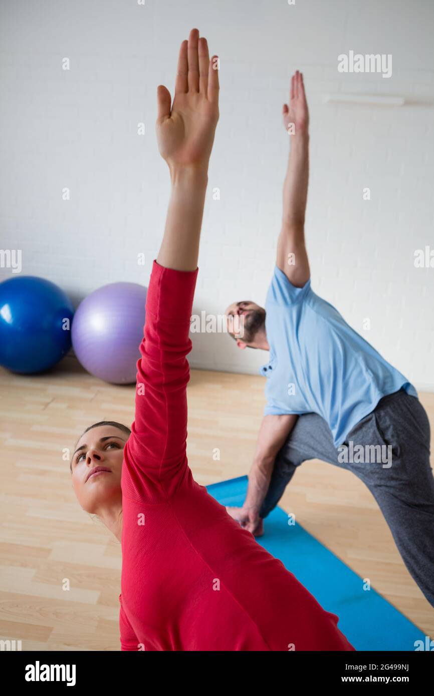 Männlicher Instruktor mit Schüler, der im Fitnessclub Triange Pose praktiziert Stockfoto