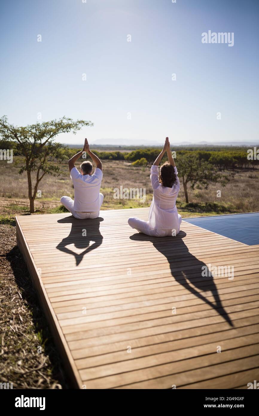 Rückansicht eines Paares, das Yoga auf einer Holzplanke praktiziert Stockfoto