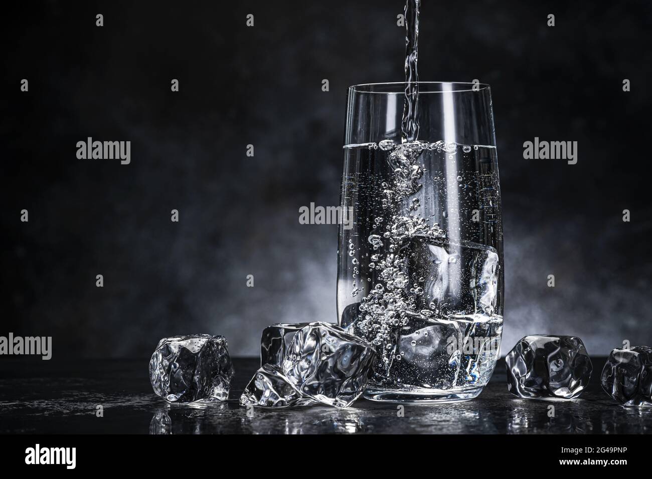 Wasser aus der Flasche in Glas auf schwarzem Hintergrund gießen Stockfoto