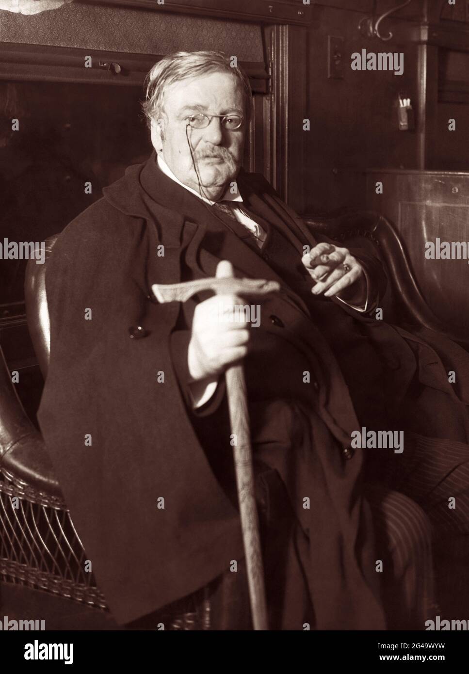 Der britische Schriftsteller G.K. (Gilbert Keith) Chesterton (1874-1936) sitzt mit Umhang, Schwertstock und Zigarre im Mai 1931. (UK) Stockfoto