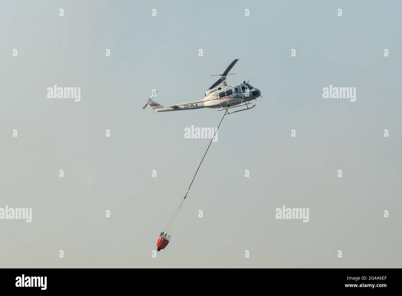 Feuerlöschhubschrauber gegen einen rauchgefüllten Himmel mit einem Wassereimer zum Nachfüllen von Konzeptfeuer und Notfallalarm, Kapstadt, Südafrika Stockfoto
