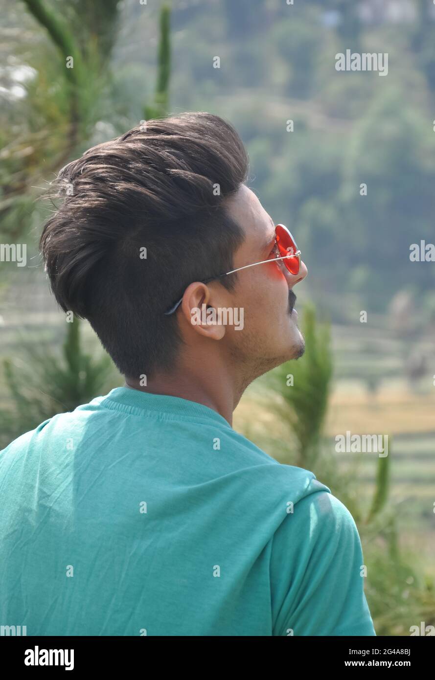 Blick von hinten auf einen hübschen indischen jungen Mann, der eine Sonnencreme trägt und im Freien in der Natur steht, während er nach oben blickt Stockfoto