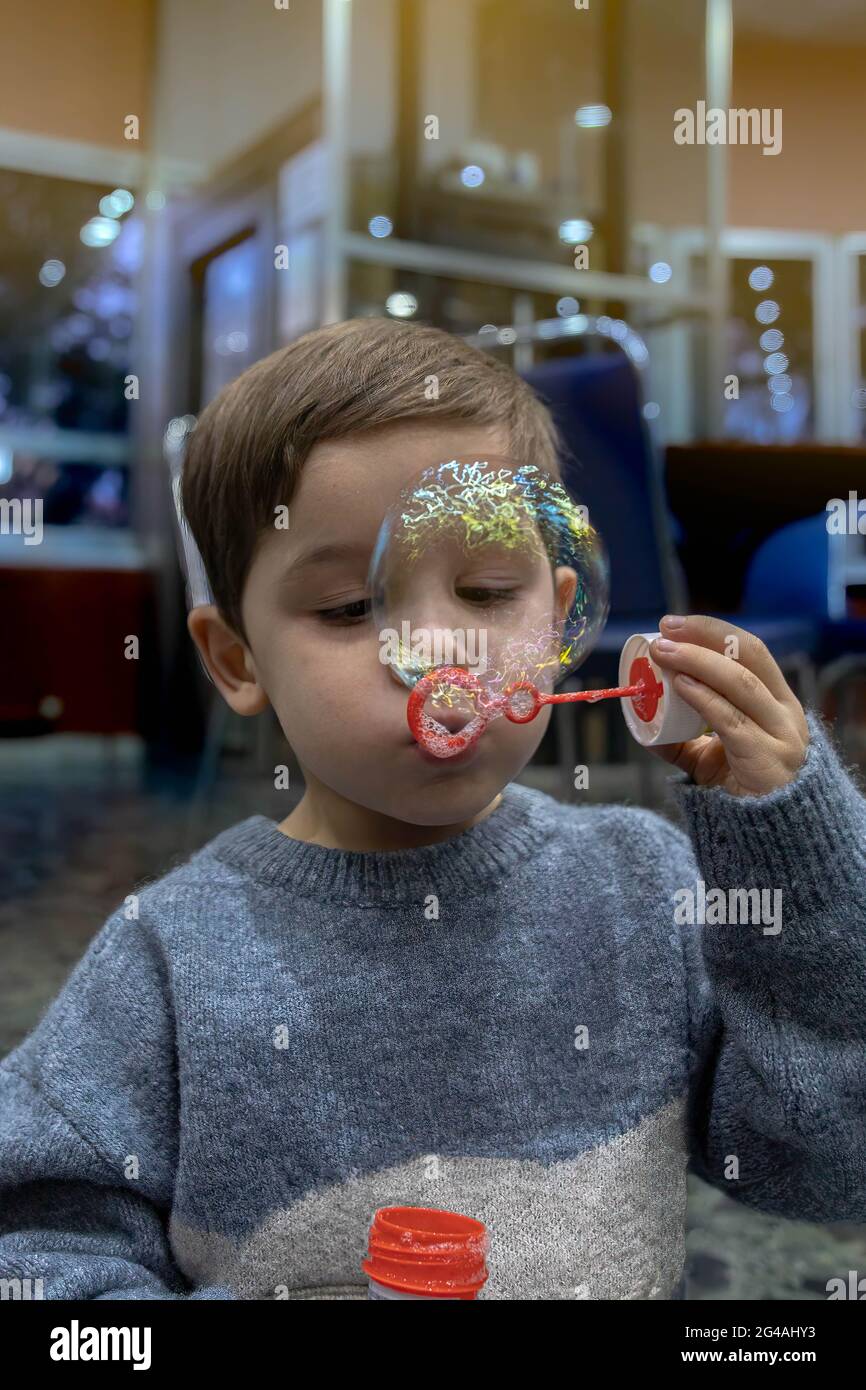 Detail eines kleinen Jungen, der durch ein Spielzeug namens Pompero bläst, um kleine und große Seifenblasen zum Spaß und Spielen zu machen. Stockfoto