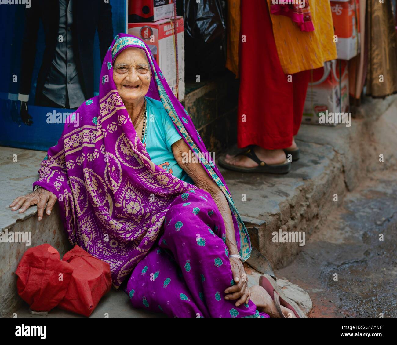 Ältere Frau in farbenfrohen traditionellen indischen Kleidern, die sich vom Spaziergang entlang der Straße in Delhi, Indien, ausruhen. Stockfoto