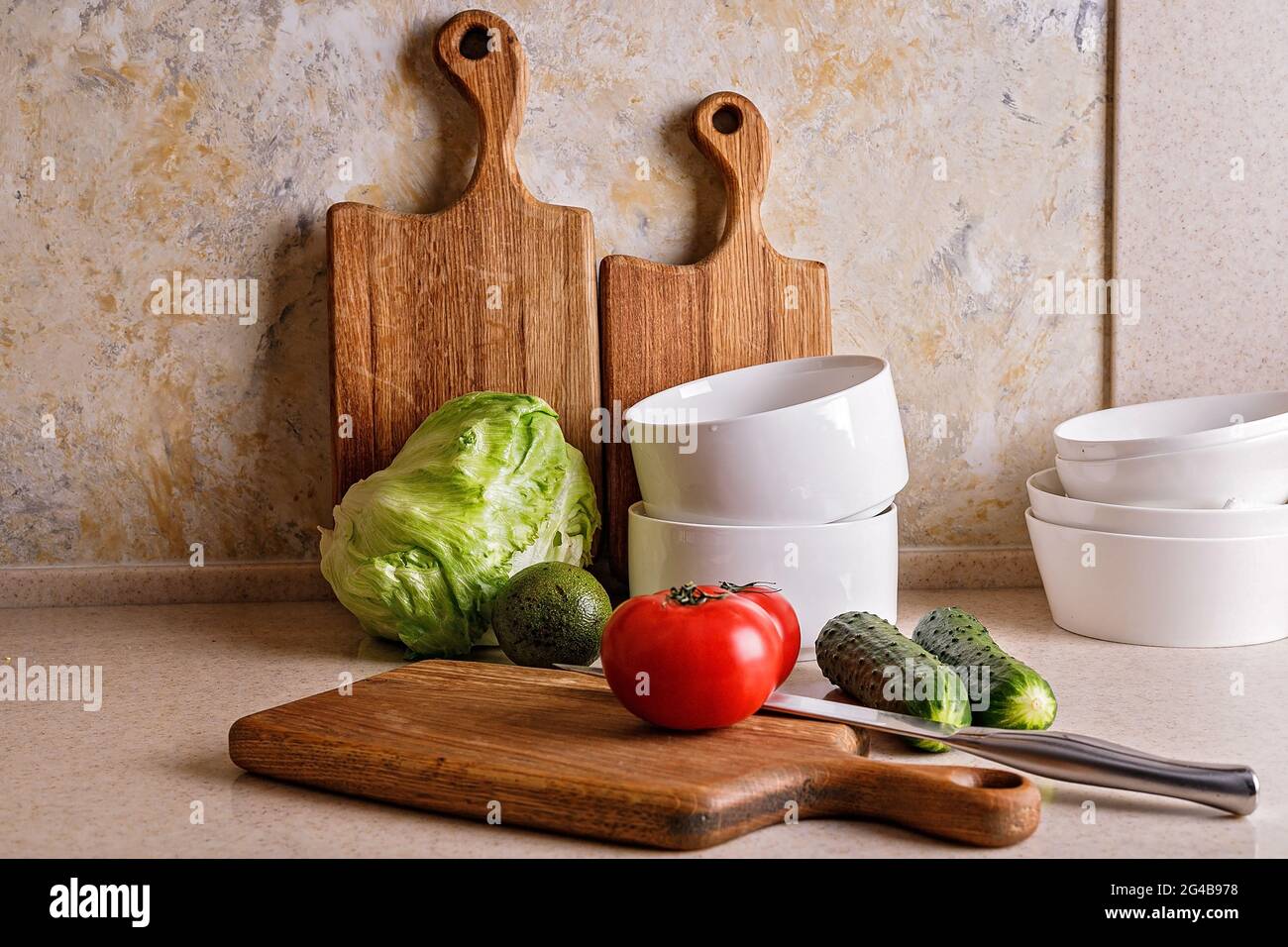 Leckeres und gesundes Gemüse. Küchenzubehör. Schneiden von Holzbrettern und Utensilien. Reife Tomaten, frische Gurken und knuspriger Eissalat, avoca Stockfoto