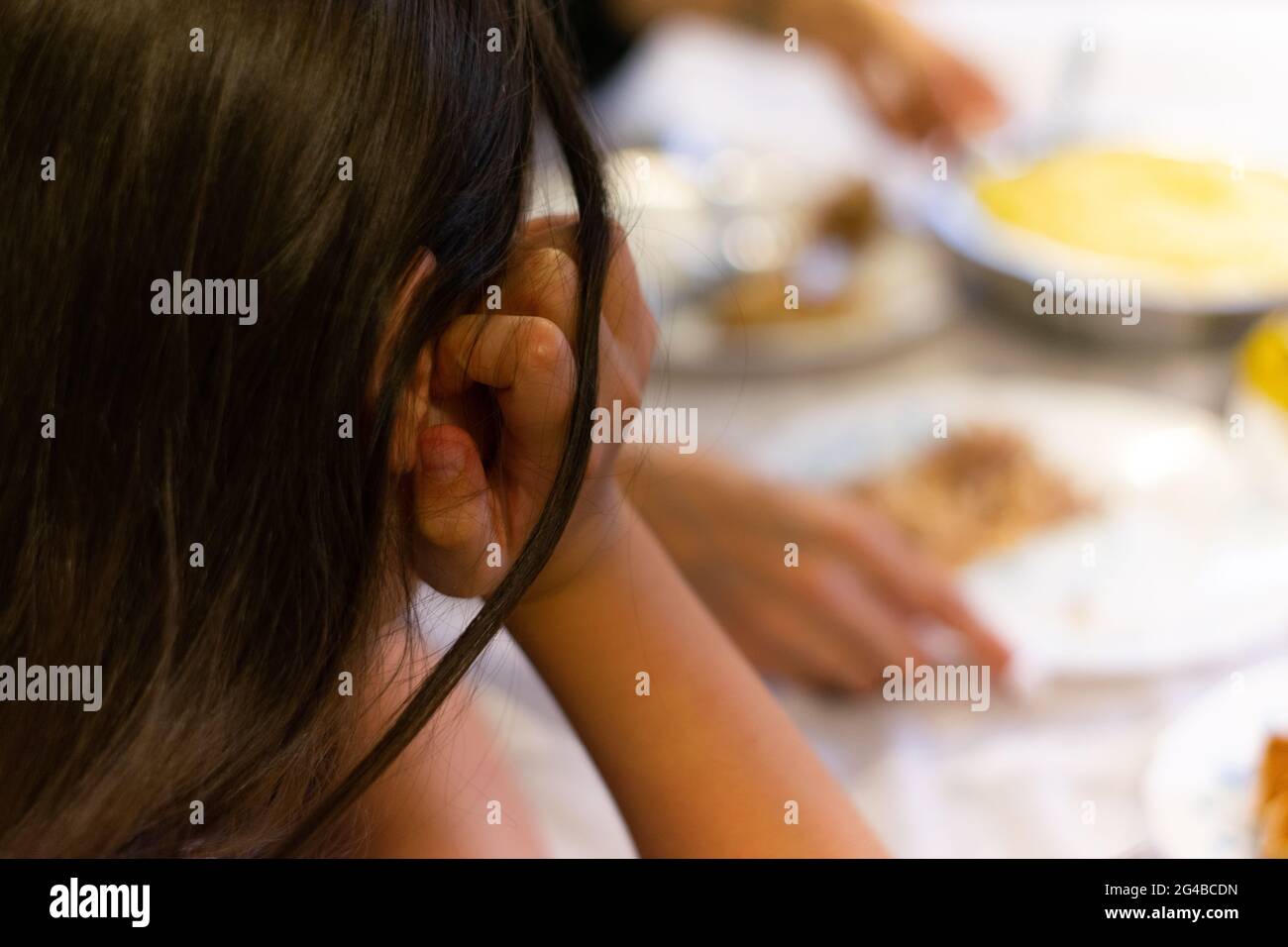 Junges Mädchen am Tisch, das beim Abendessen Teller ansah, Familienleben. Kinder am Tisch ruhen sich aus Stockfoto