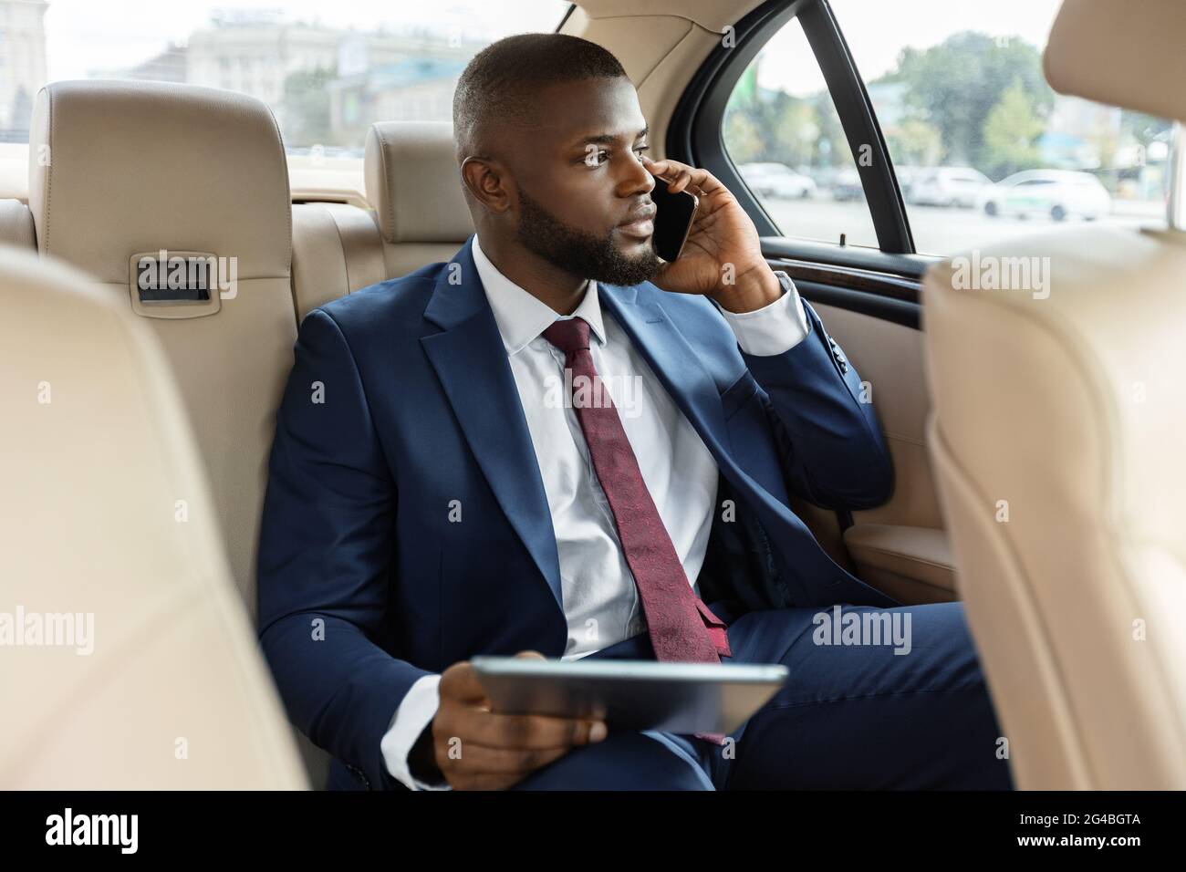 Wohlhabender schwarzer Manager, der im Auto sitzt und ein digitales Tablet verwendet Stockfoto