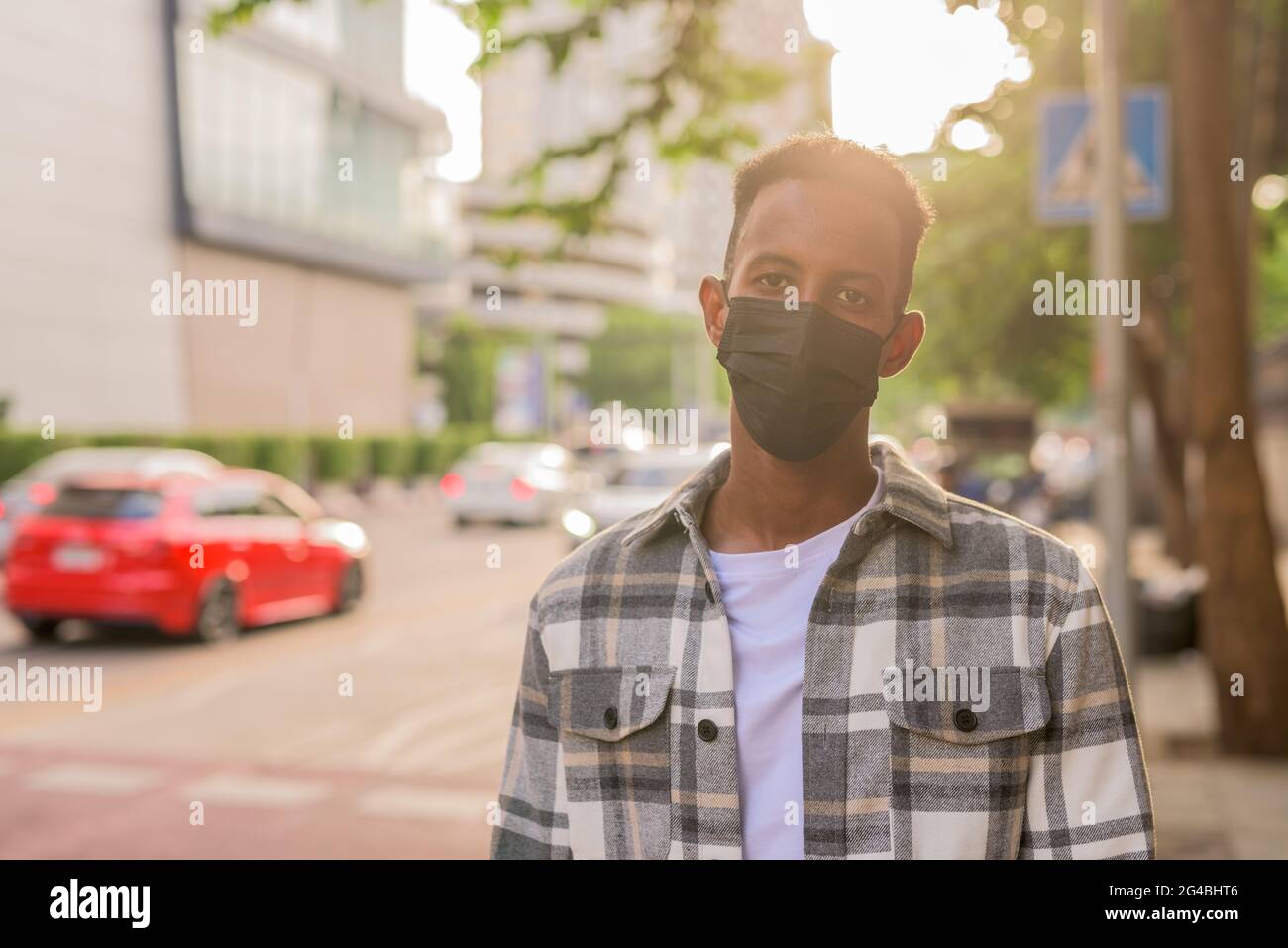 Schöner und modischer afrikanischer schwarzer Mann im Sommer in der Stadt trägt Gesichtsmaske hinten beleuchtet Aufnahme mit Linse Flare Stockfoto