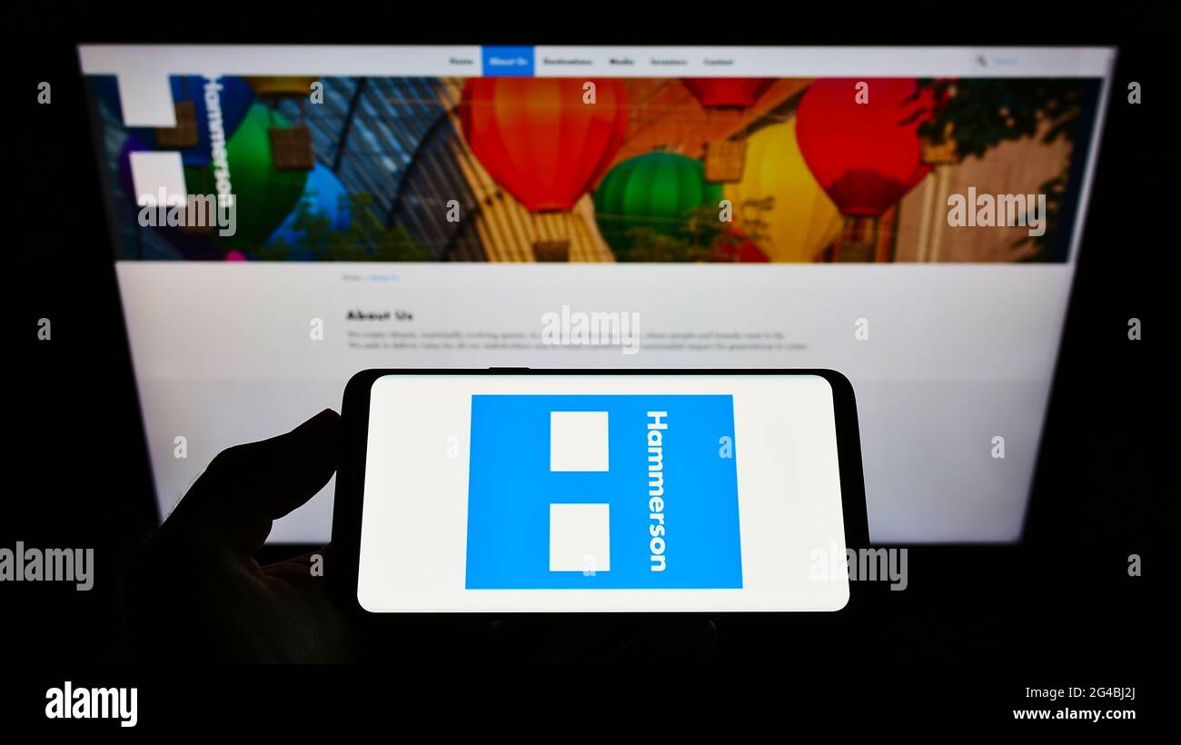 Person mit Mobiltelefon und Logo des britischen Immobilienentwicklungsunternehmens Hammerson plc auf dem Bildschirm vor der Webseite. Konzentrieren Sie sich auf die Telefonanzeige. Stockfoto