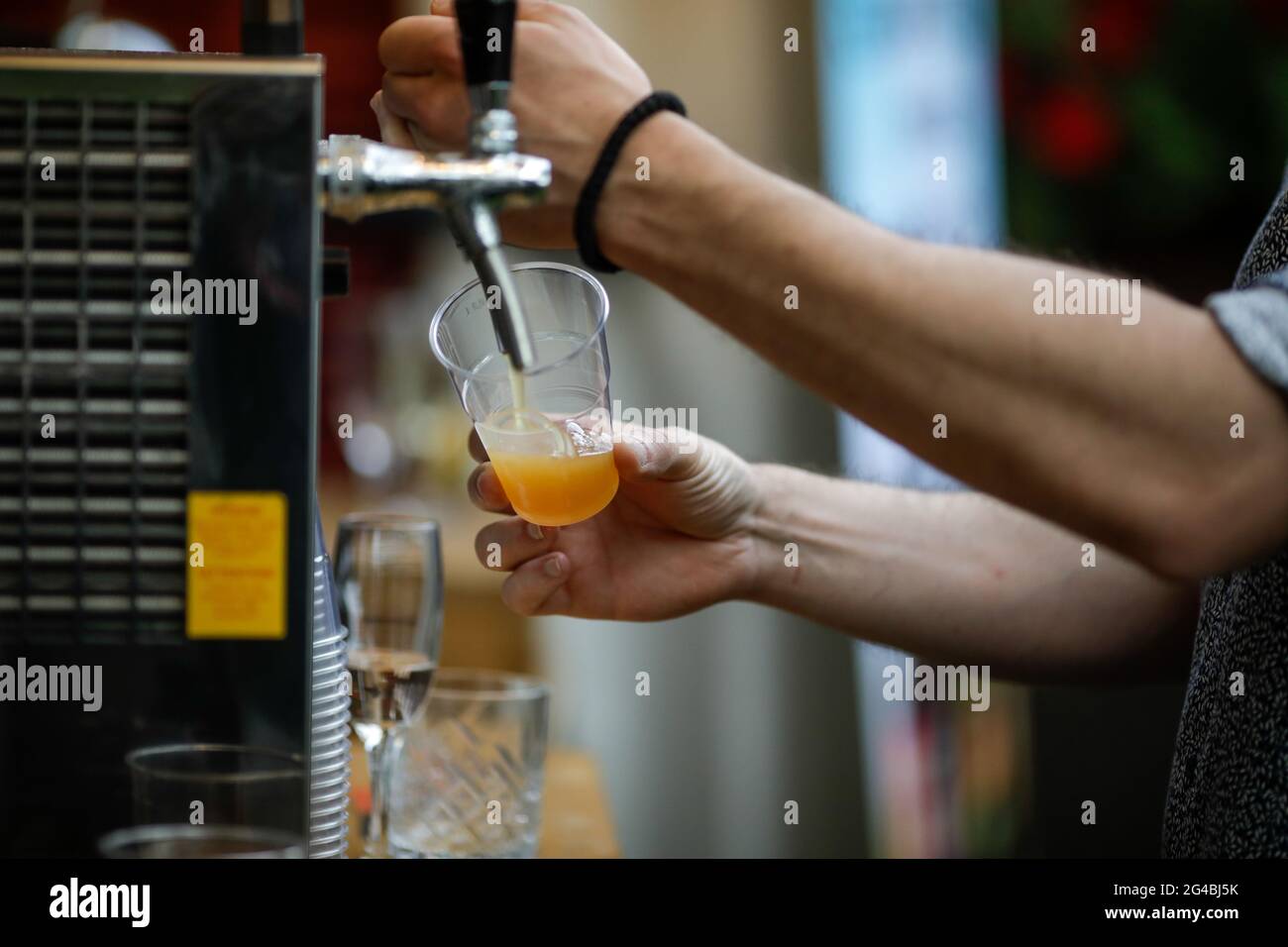 Bild mit geringer Schärfentiefe (selektiver Fokus) mit einem Mann, der Craft-Bier aus einem Spender in ein Kunststoffglas gießt. Stockfoto