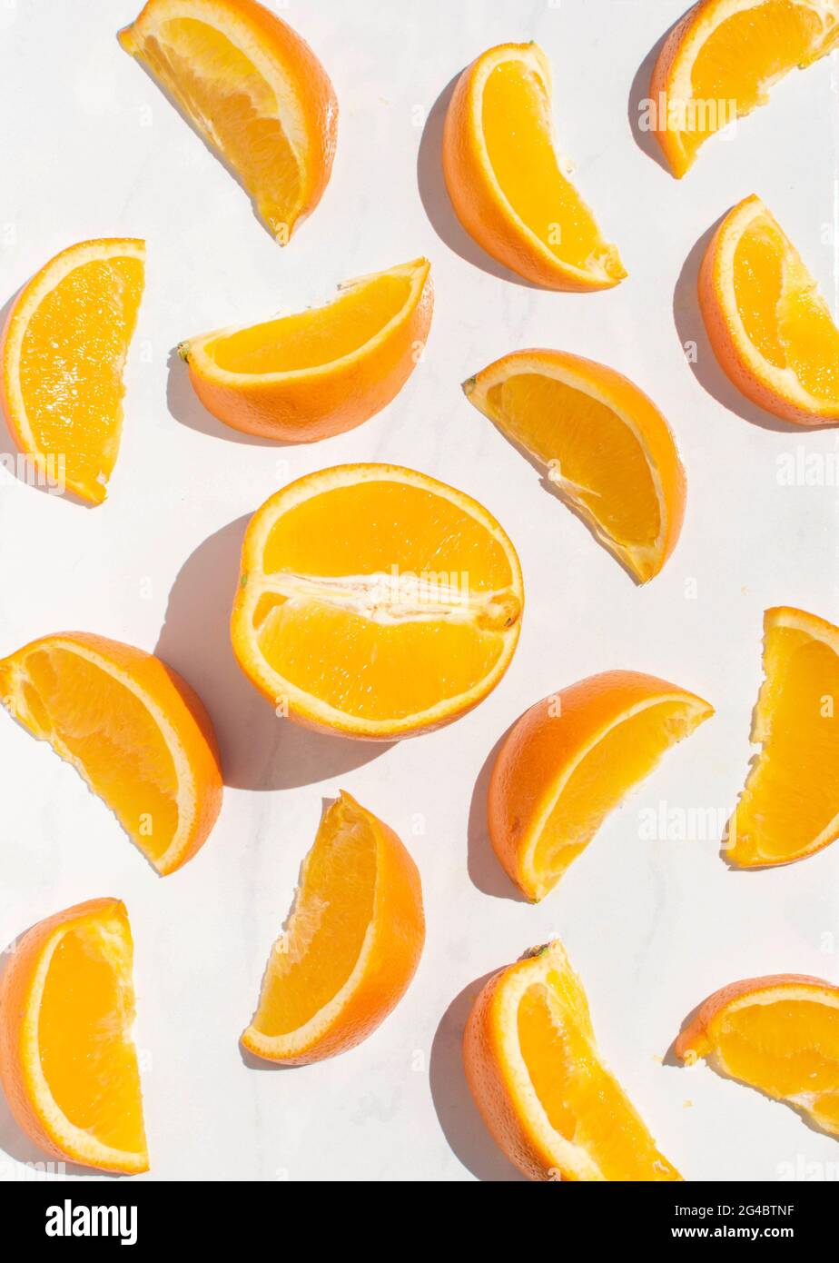 Flache Lay-Komposition aus oranger Hälfte mit orangefarbenen Scheiben, die auf einem weißen Marmorhintergrund in der hellen Sommersonne angeordnet sind. Stockfoto