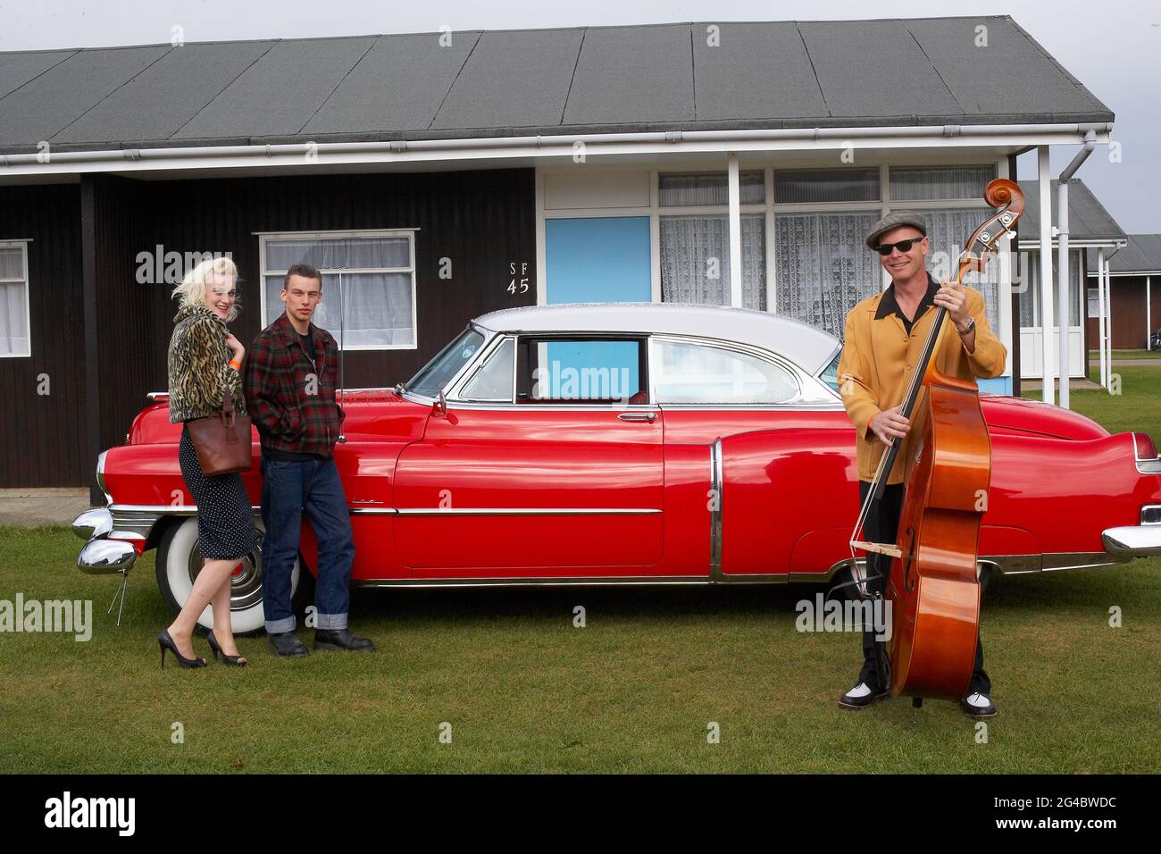 GROSSBRITANNIEN / England /Norfolk /Hemsby Rock 'N' Roll Weekender. Ein Paar und ein Kontrabasser posieren neben einem roten cadillac. Stockfoto