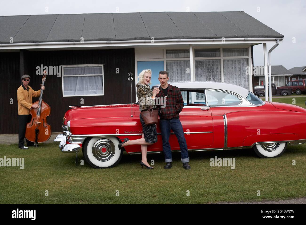 GROSSBRITANNIEN / England /Norfolk /Hemsby Rock 'N' Roll Weekender. Ein Paar und ein Kontrabasser posieren neben einem roten cadillac. Stockfoto