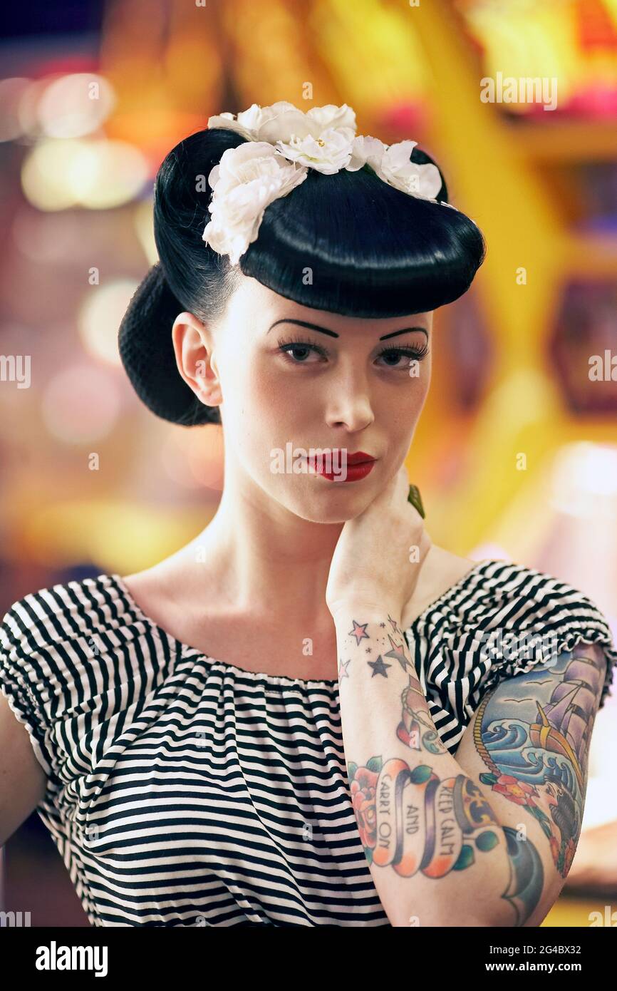 Rockabilly Girl posiert mit ihren Tattoos im Vergnügungspark mit Neonschildern im Hintergrund. Stockfoto