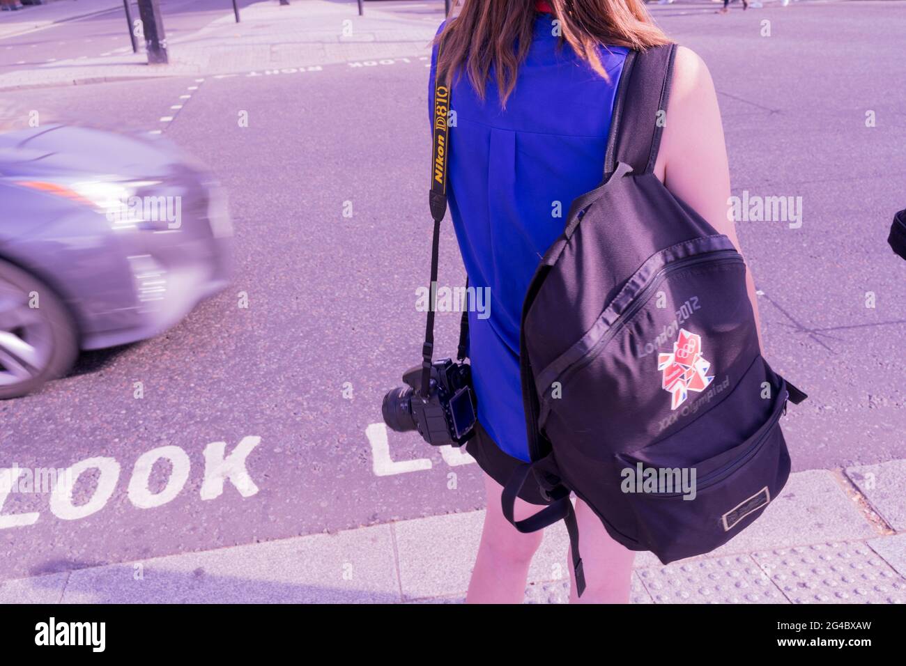 Frau in blauer Spitze trägt London 2012 Rucksack, der an Fußgängerübergangsampeln wartet, um grün zu werden, London trafalgar Square, England, Großbritannien Stockfoto