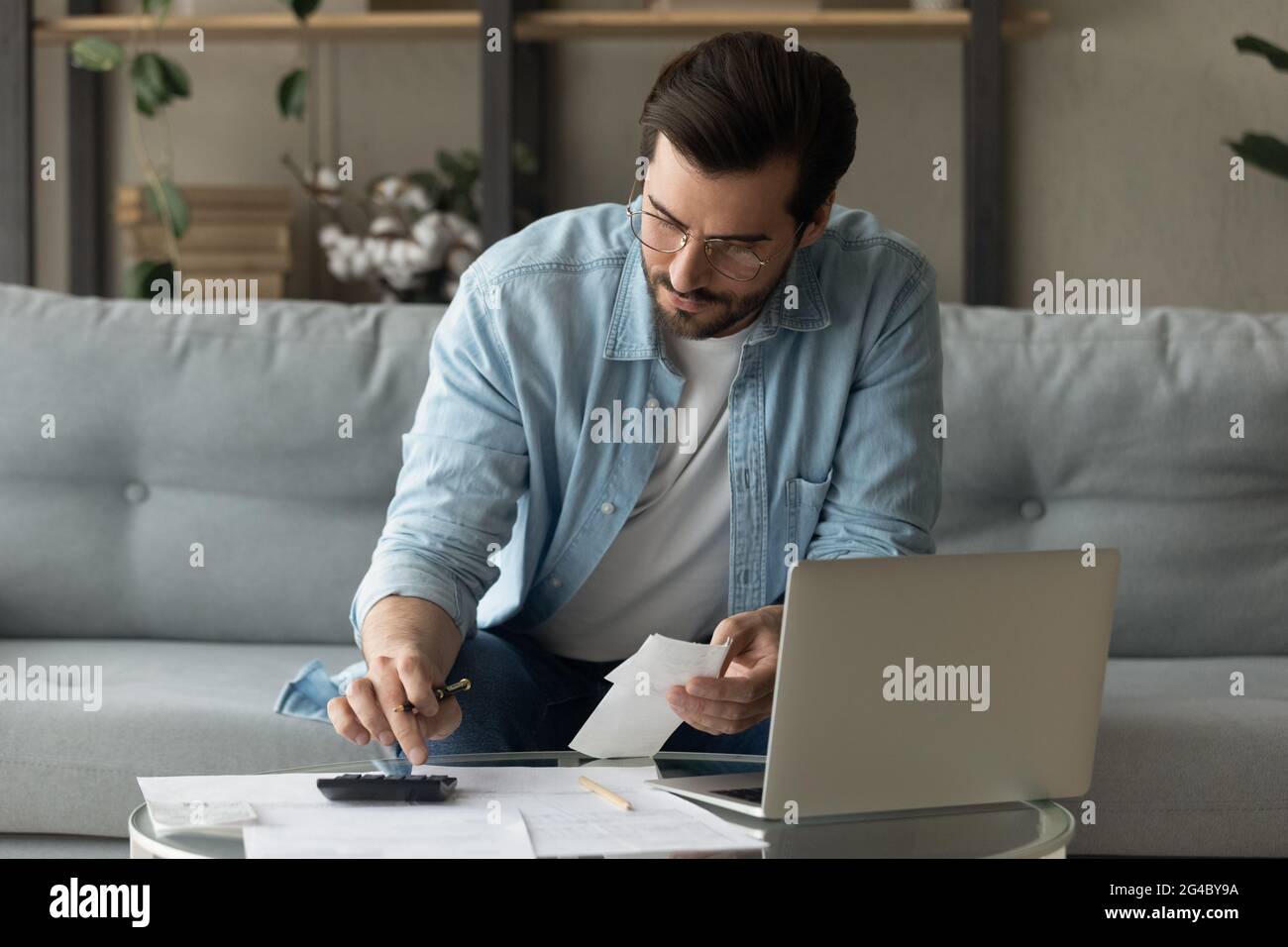 Konzentrierter junger Mann aus den 30er Jahren in Brillen, der die Ausgaben berechnet. Stockfoto