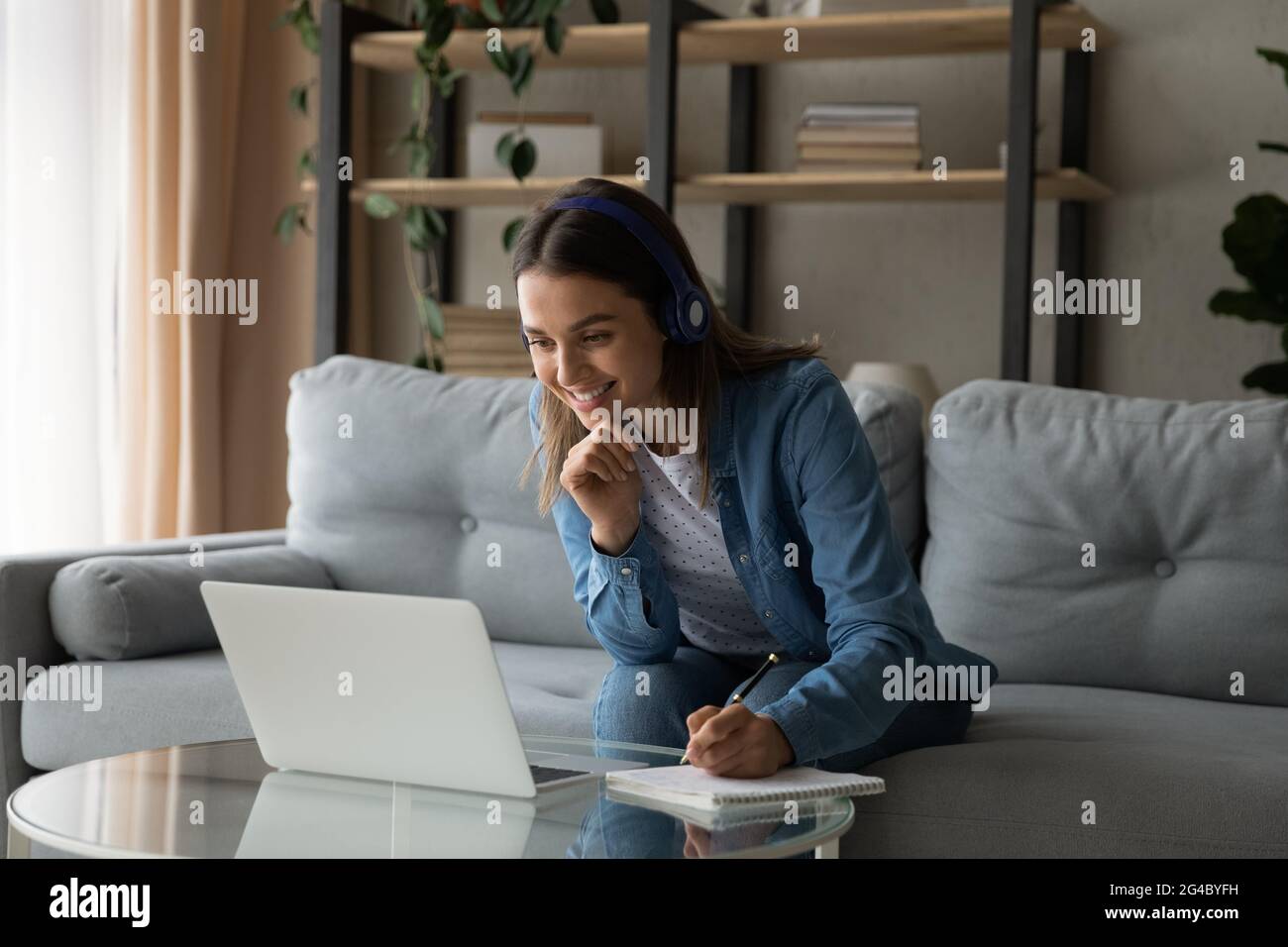 Glückliche junge Frau mit Kopfhörern, die Online-Kurse besuchen. Stockfoto