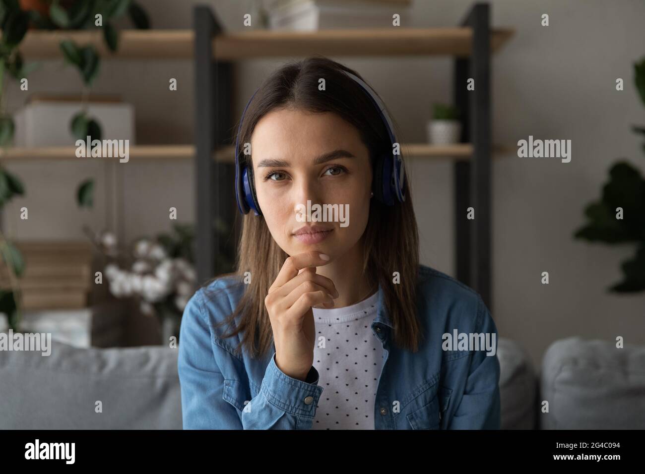 Nachdenkliche junge Frau mit Kopfhörern, die die Kamera anschaut. Stockfoto