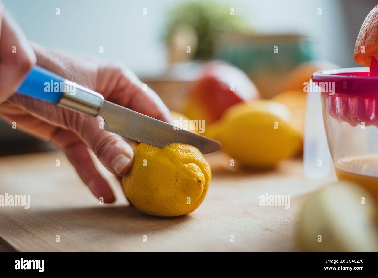 Eine Frau, die mit einem blauen Messer auf einem Holztisch, umgeben von anderen Früchten, eine Zitrone schneidet. Stockfoto