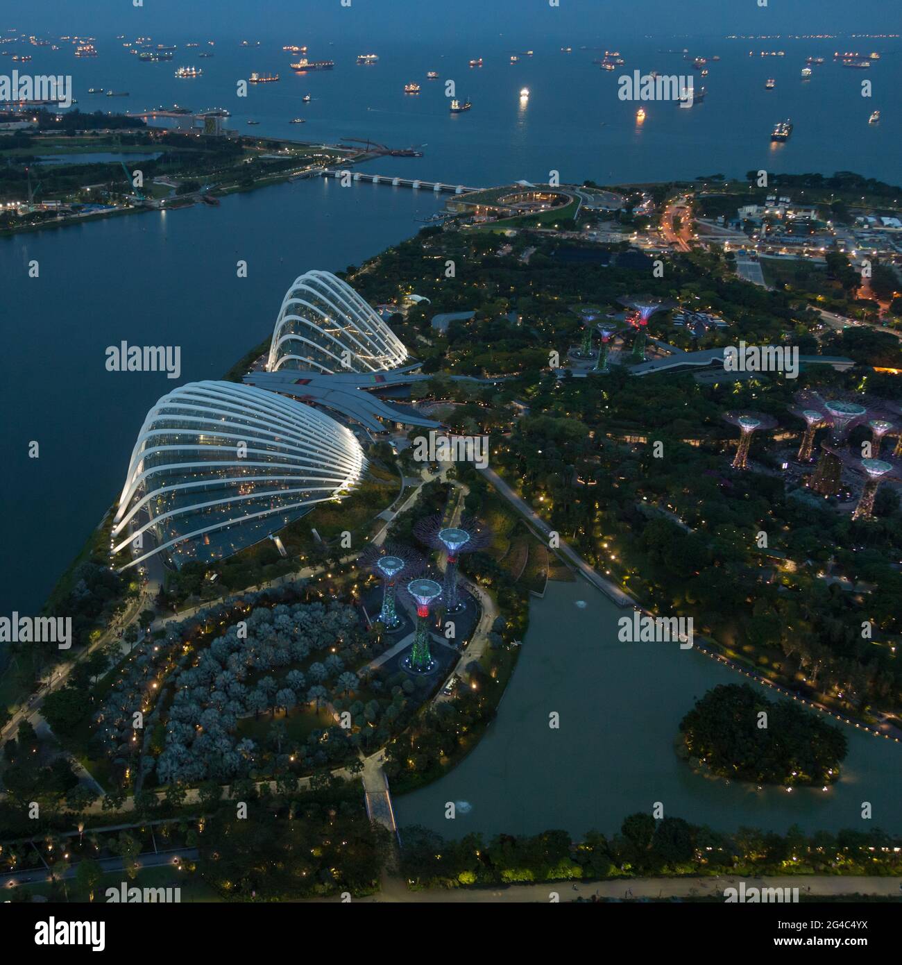 Blick auf die Gärten von Singapur an der Bucht, wenn die Sonne untergeht und die Lichter aufgehen, mit vielen Schiffen in der geschäftigen Straße von Singapur dahinter Stockfoto