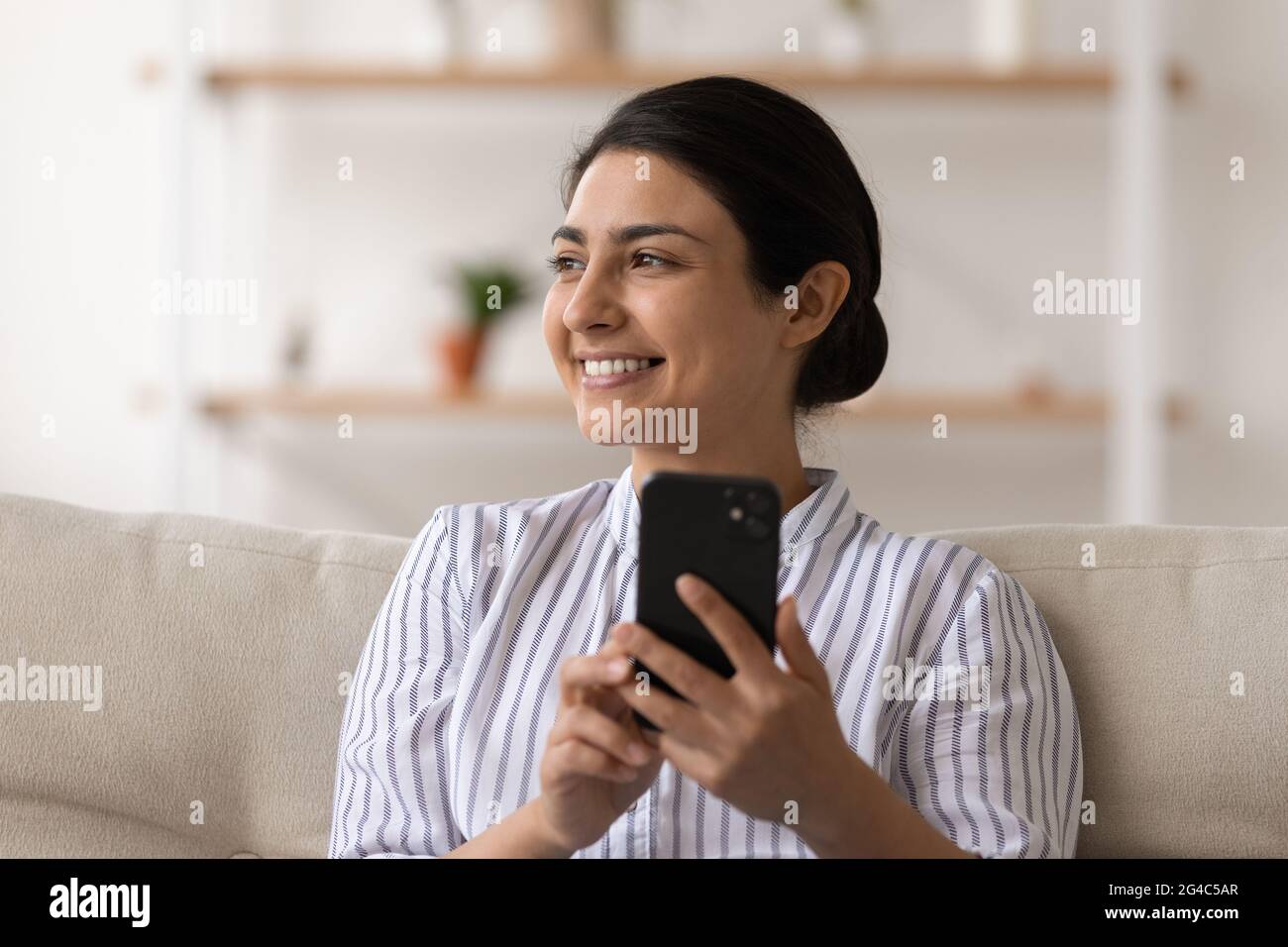 Lächelnde indische Frau verwenden Smartphone zu Hause entspannen Stockfoto
