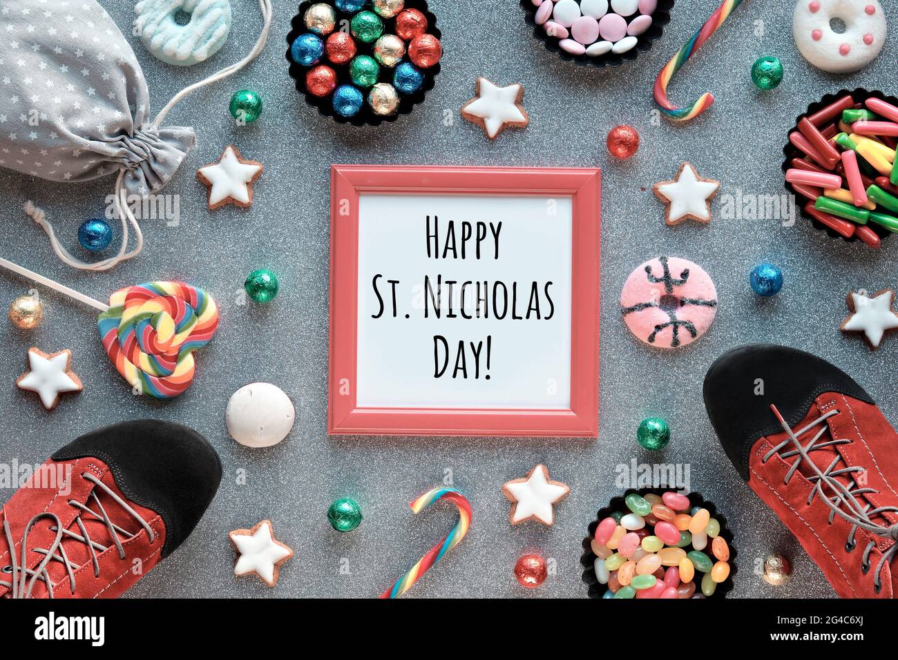 Text Happy St. Nicolas Day in rotem Rahmen. Traditioneller Feiertag in Deutschland und Westeuropa am 6. Dezember. Verschiedene Süßigkeiten, Süßigkeiten, Kekse und ein Paar Stockfoto