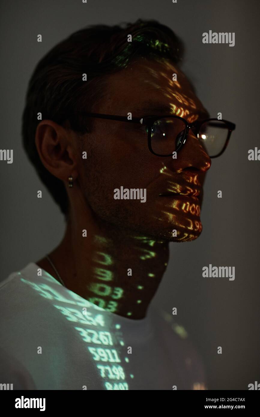 Dunkles Porträt eines jungen Mannes in einer Brille mit Computercode im Gesicht Stockfoto