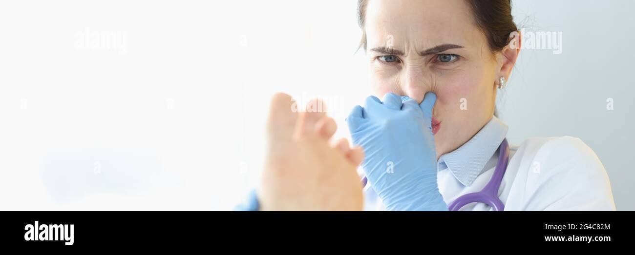 Arzt Dermatologe hält Patienten Fuß und bedeckt die Nase mit der Hand Stockfoto