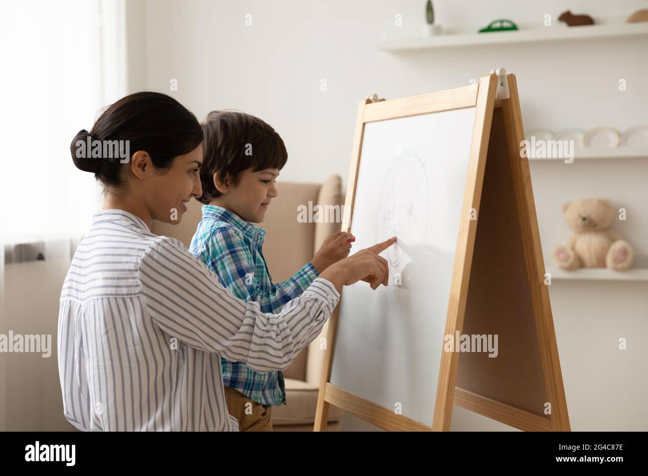 Glückliche indische Mutter und kleiner Sohn zeichnen auf Whiteboard Stockfoto