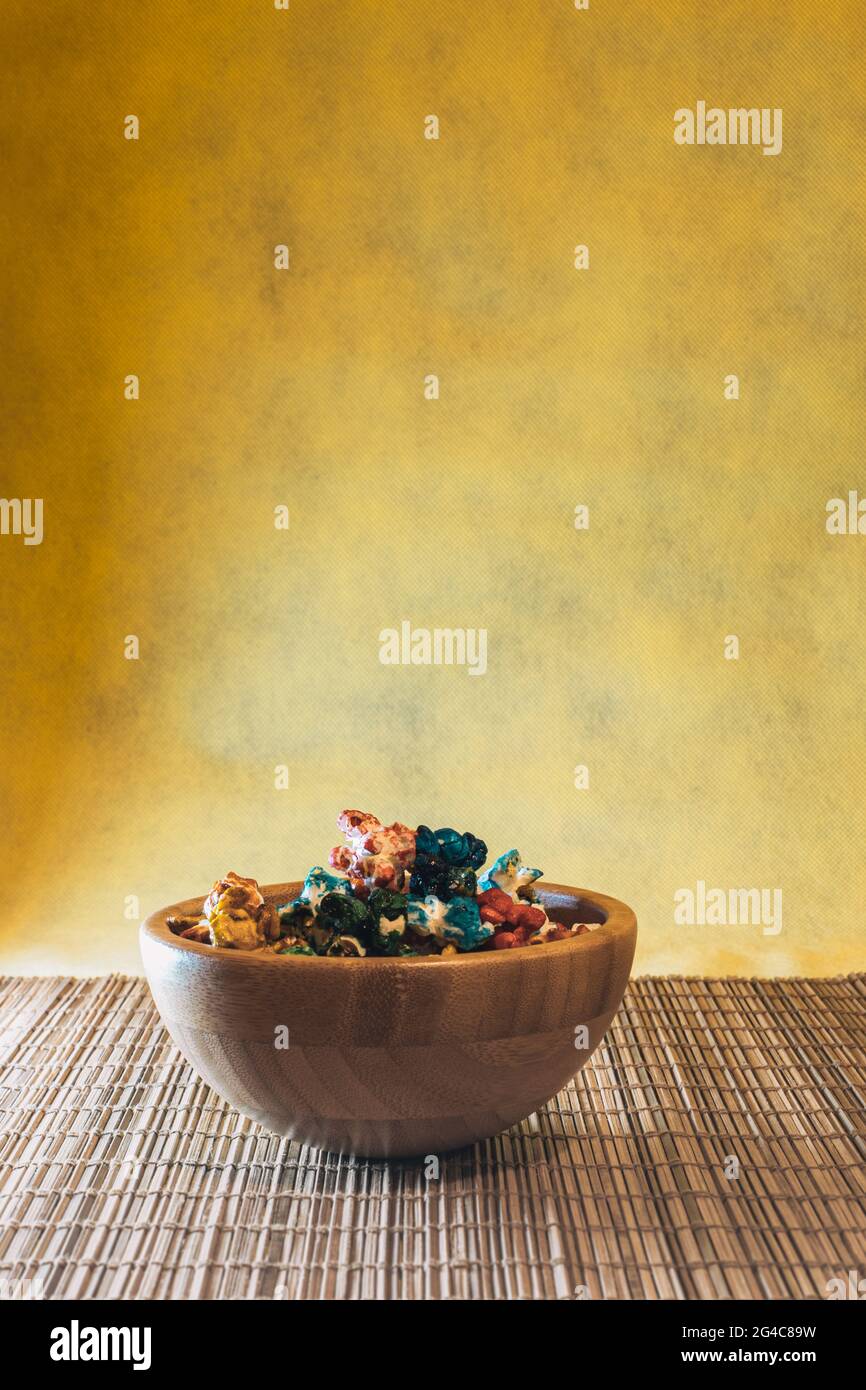 Bambusholz-Schale mit buntem, süßem Popcorn mit gelbem Hintergrund und Kopffelder Stockfoto