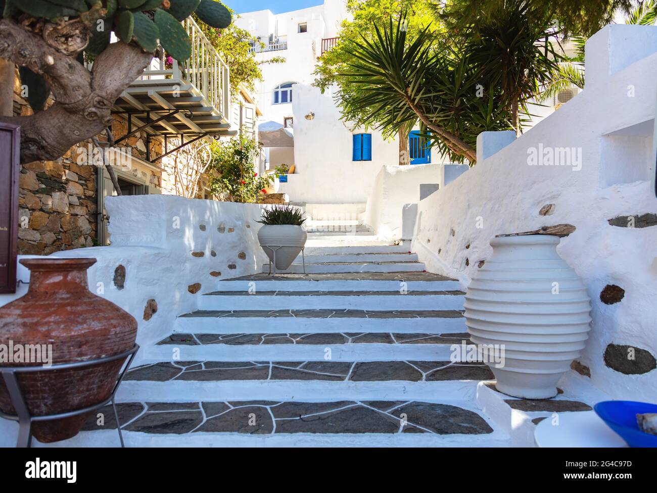 Häuser mit weiß getünchten Wänden Sommer sonnigen Tag auf Sifnos Insel, Griechenland. Alte leere traditionelle schmale Steintreppe von unten zum oberen großen Keramiktopf Stockfoto