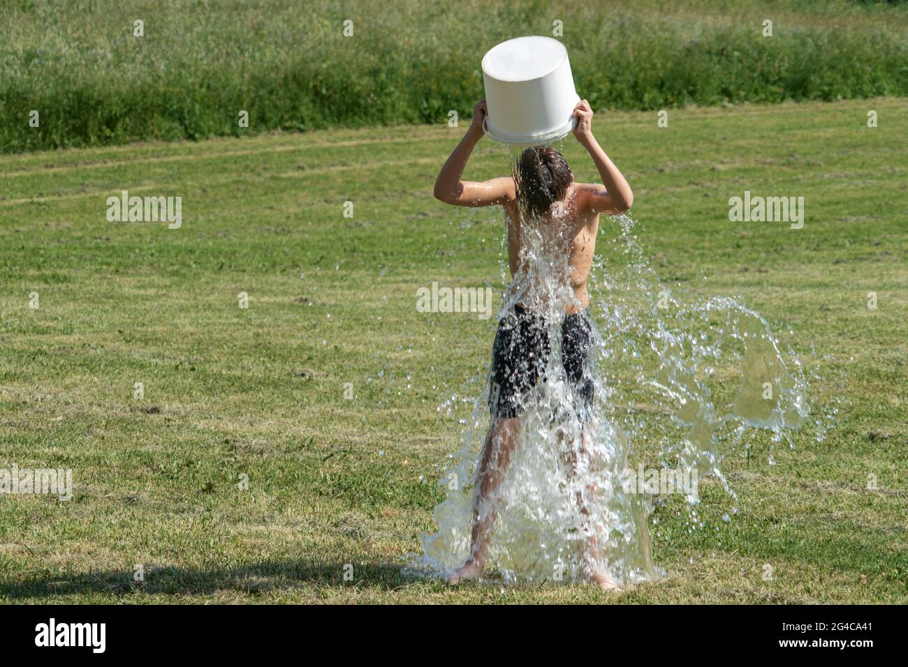 Teenager gießt draußen einen Eimer mit kaltem Wasser über seinen Kopf.  Eiswasser Herausforderung. Vorteile der Kaltwassertherapie Stockfotografie  - Alamy